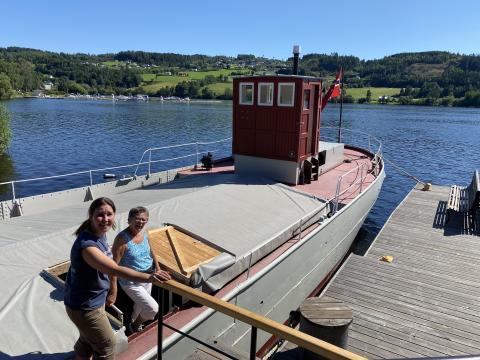 I juli 2024 var det åpen dag på MS Brandbu. Grethe Johnsrud fra Randsfjordsmuseet, til venstre,  ga info i sommersola til Ingeborg Rækstad og fotograf Inger Stensrud Haug. 