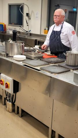 Kokk står bak kjøkkenøy og forklarer