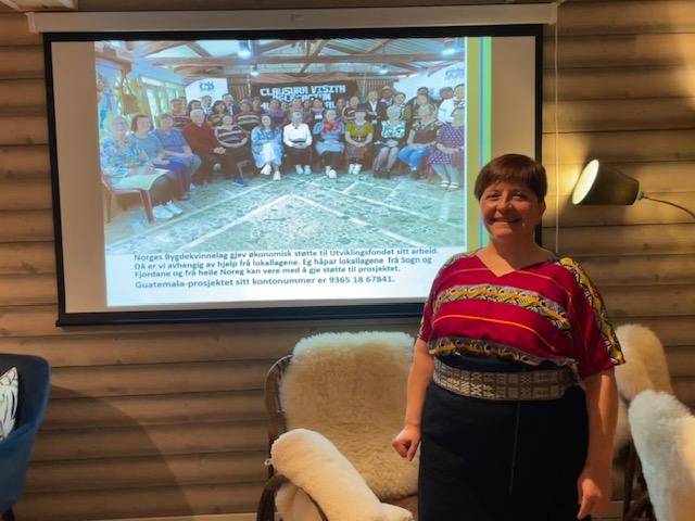 Cecilie Lyslo i nasjonaldrakt frå Guatemala, framfor lerret med presentasjon om Guatemala.