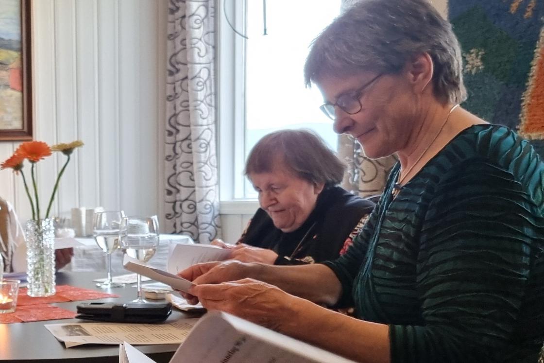 To kvinner blar frem sanger i et hefte