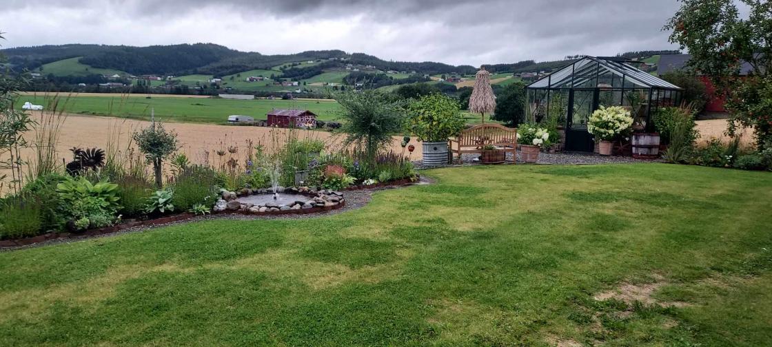 Hage med drivhus, bed, liten dam med fontene