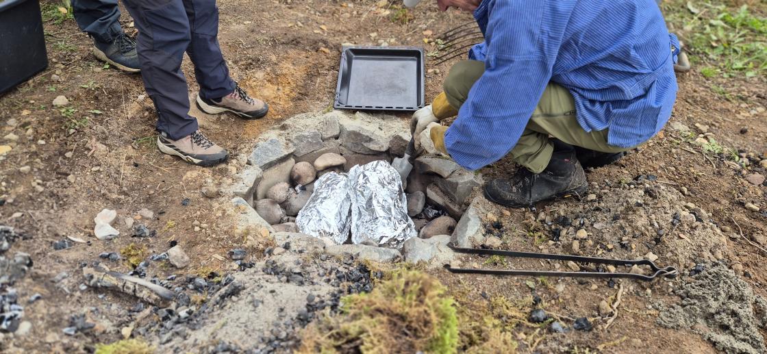 Pakkene med kjøttet blir dekket med varme steiner, sand og grus og mose på toppen.